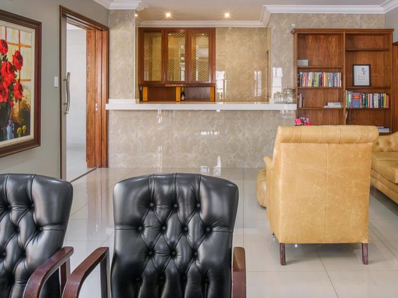 A well-maintained home bar area featuring a marble-clad counter, built-in wooden cabinetry, and polished tile flooring, creating a sophisticated entertainment space.