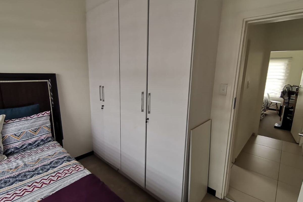A bedroom featuring a white built-in wardrobe with modern handles and tiled flooring, leading into an adjacent room.