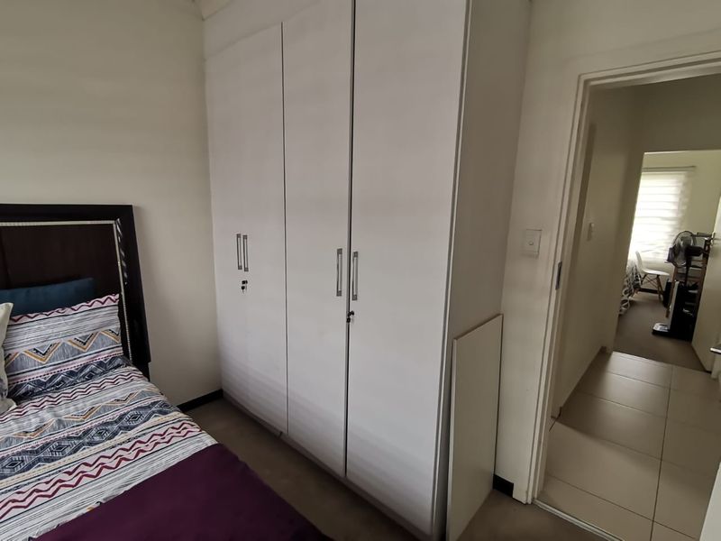 A bedroom featuring a white built-in wardrobe with modern handles and tiled flooring, leading into an adjacent room.