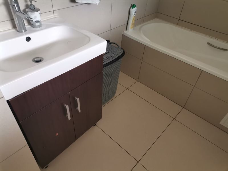 A functional bathroom featuring a vanity cabinet with a basin, chrome mixer tap, and a built-in bathtub with tiled surrounds.