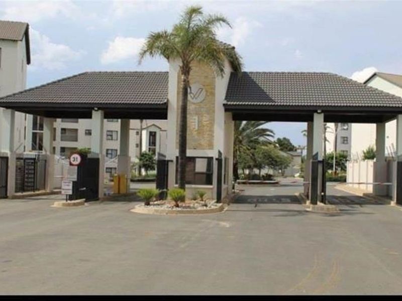 A secure apartment complex entrance featuring a gated security house, boom gates, and paved driveway access.