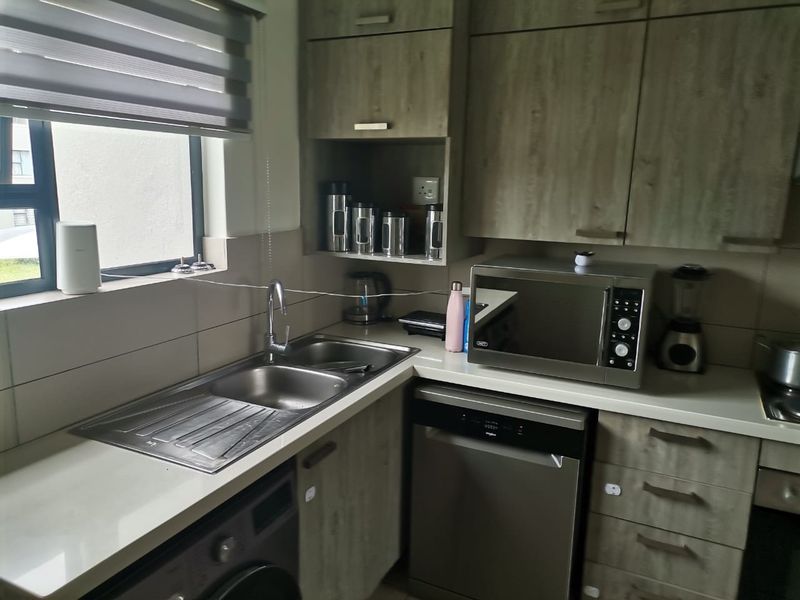 A functional kitchen featuring modern wood-look cabinetry, stone countertops, a stainless steel sink, and integrated appliances including a dishwasher and oven.