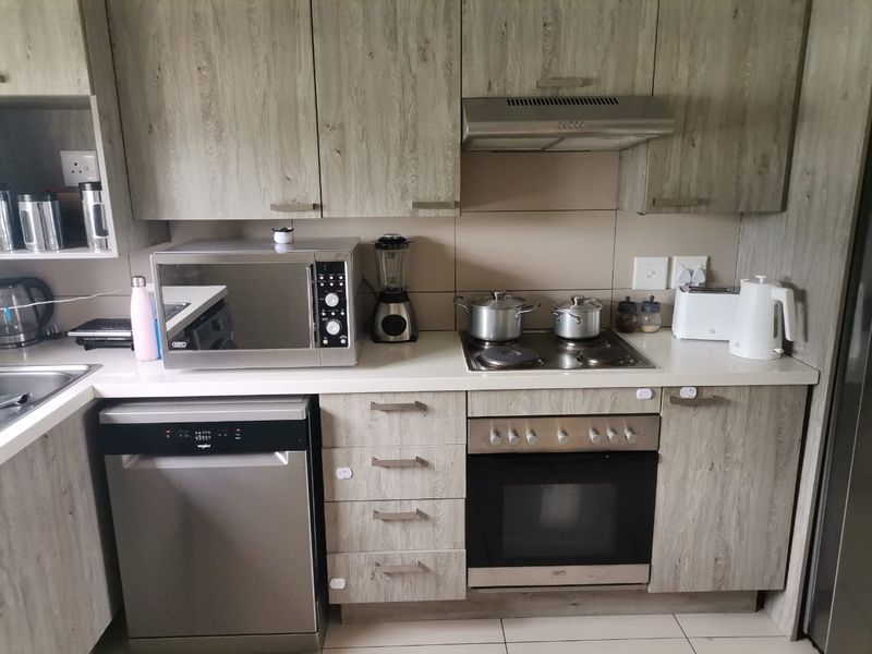 Modern kitchen featuring wood-grain cabinetry, stone-look countertops, built-in oven, electric hob, extractor fan, and integrated dishwasher.
