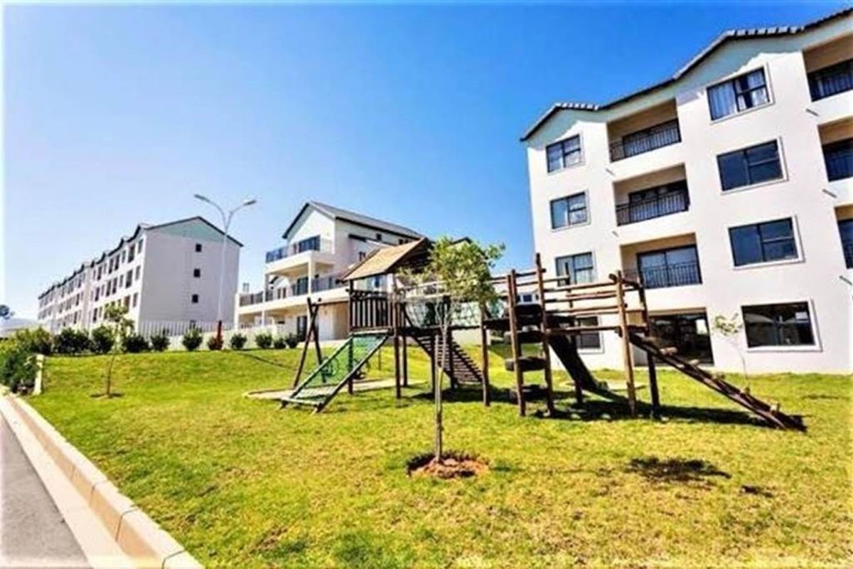 Exterior view of a multi-story apartment complex featuring landscaped grounds and a communal playground area.