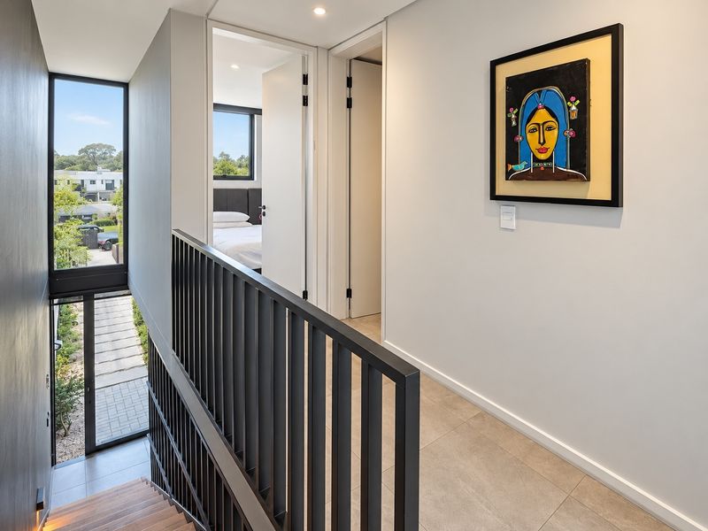 Modern upper-level hallway featuring a sleek metal balustrade, tiled flooring, and large windows overlooking the exterior, providing access to adjacent bedrooms.