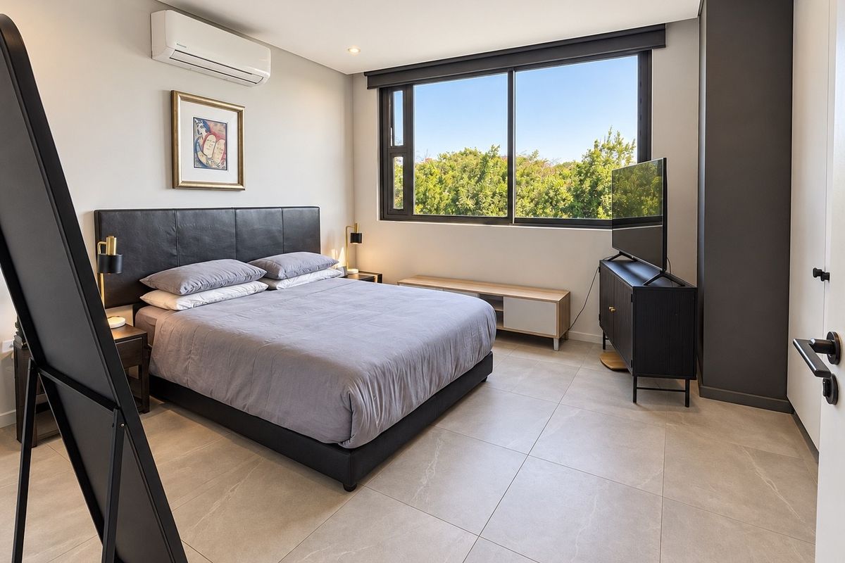 Modern bedroom featuring large format floor tiles, a split-system air conditioner, and a large window providing natural light and garden views.
