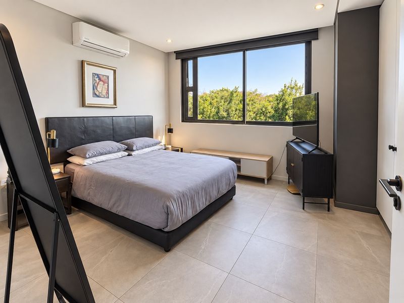 Modern bedroom featuring large format floor tiles, a split-system air conditioner, and a large window providing natural light and garden views.