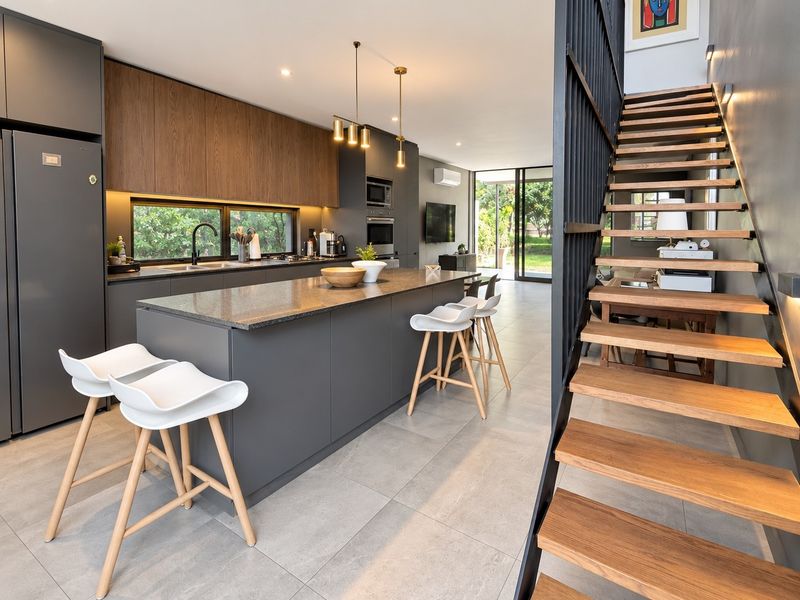 Modern open-plan kitchen featuring a central island, stone countertops, integrated appliances, and a striking floating staircase leading to the upper level.