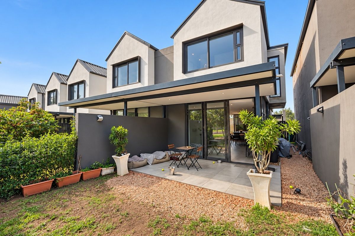 Rear view of a modern townhouse featuring a covered tiled patio, sliding glass doors, and a private garden area.