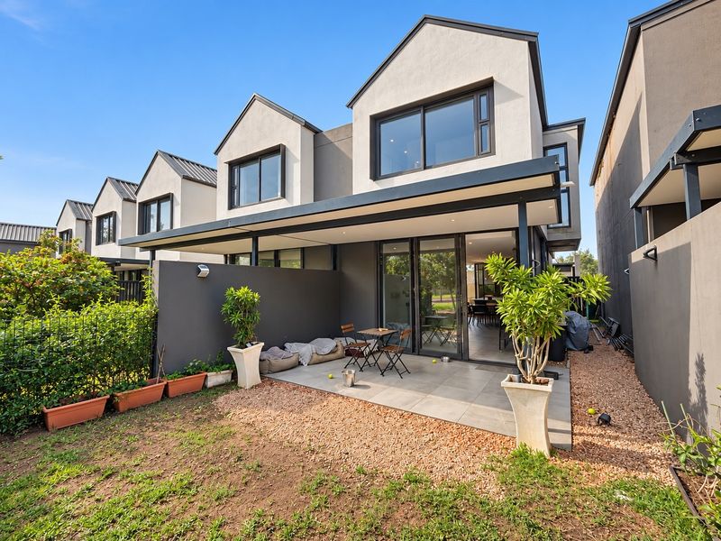 Rear view of a modern townhouse featuring a covered tiled patio, sliding glass doors, and a private garden area.
