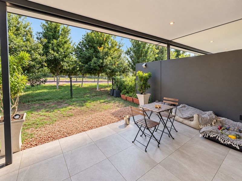 A modern covered patio featuring large format floor tiles, recessed lighting, and a private wall, overlooking a landscaped garden area.