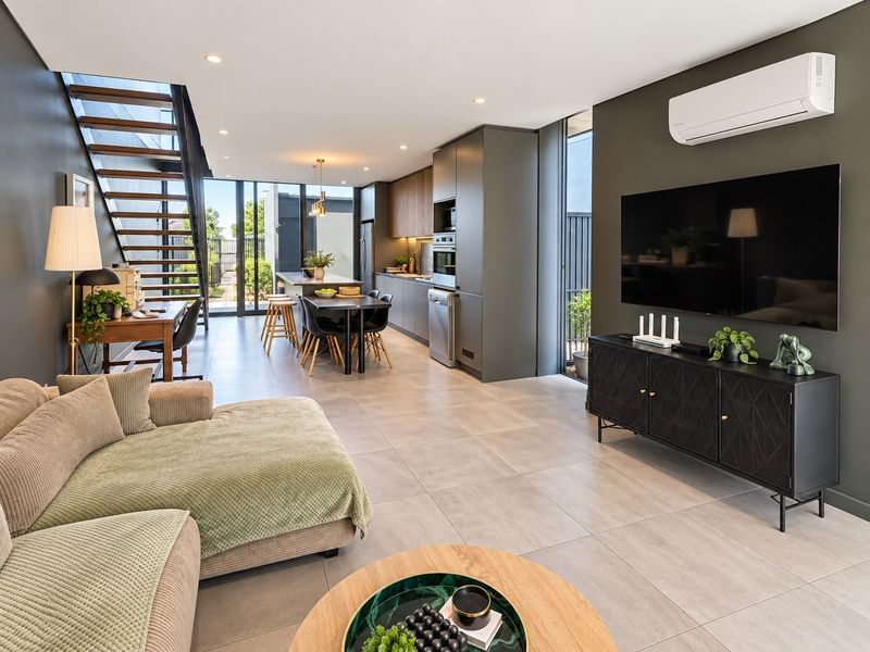 Modern open-plan living area featuring a sleek kitchen with integrated appliances, tiled floors, a feature staircase, and direct access to the outdoor space.