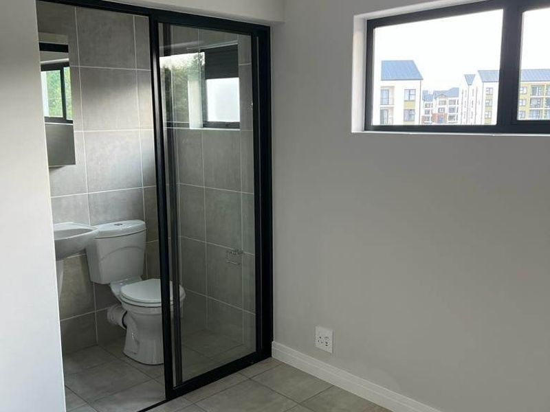 A modern, empty bedroom featuring neutral tiled floors, a sleek black-framed sliding door leading to an en-suite bathroom, and contemporary finishes.