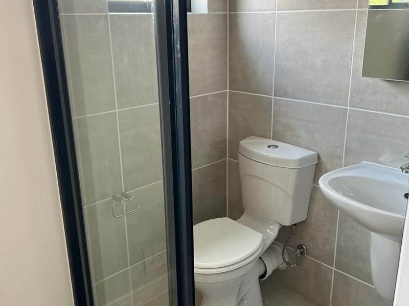 A clean, modern bathroom featuring a glass-enclosed shower, pedestal basin, and neutral wall and floor tiling.