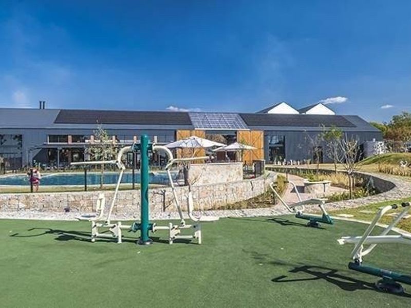 Outdoor fitness area featuring fixed exercise equipment, adjacent to a swimming pool and landscaped gardens within a modern residential complex.