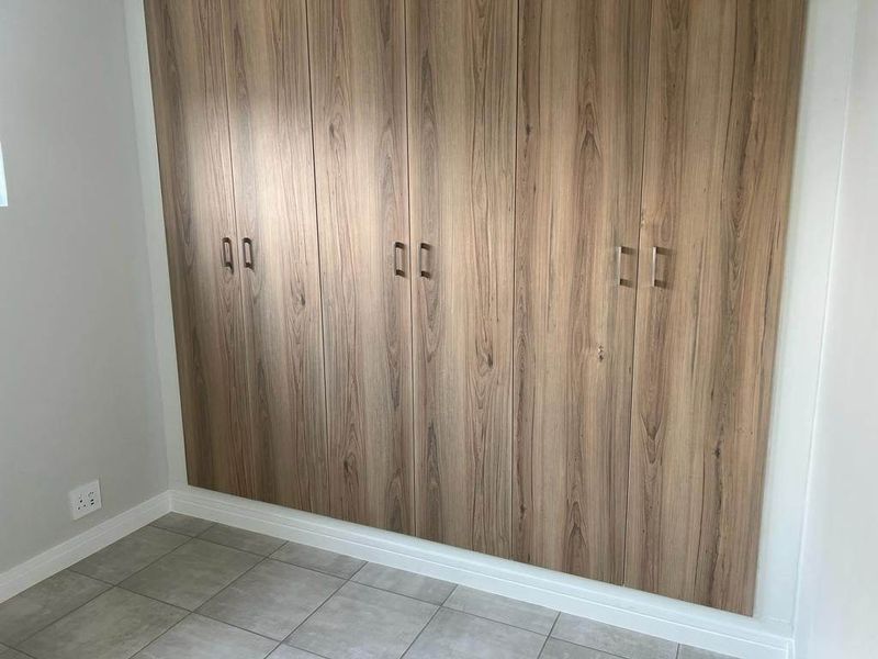 A clean, modern bedroom featuring floor-to-ceiling wood-grain built-in cupboards and neutral tiled flooring.