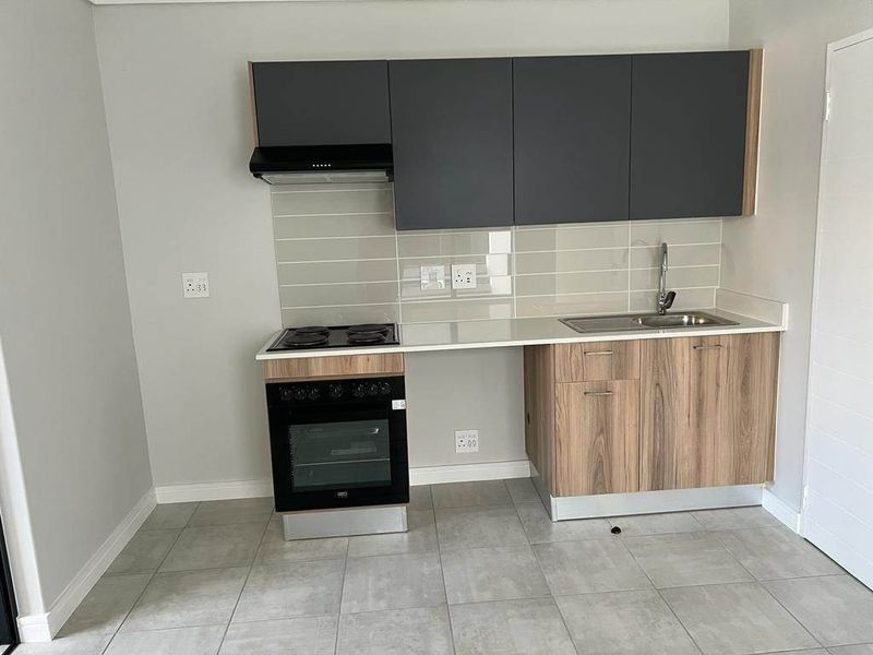 Modern kitchen featuring sleek grey and wood-tone cabinetry, built-in oven, electric hob, extractor fan, and a stainless steel sink with tiled backsplash.