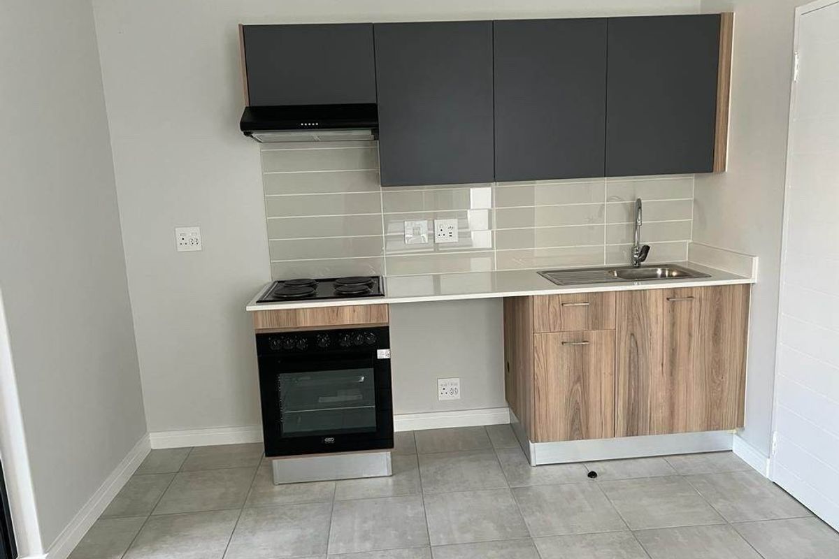Modern kitchen featuring sleek grey and wood-tone cabinetry, built-in oven, electric hob, extractor fan, and a stainless steel sink with tiled backsplash.