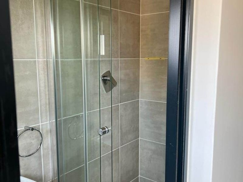 A clean, modern bathroom featuring a glass-enclosed shower with neutral wall and floor tiling.