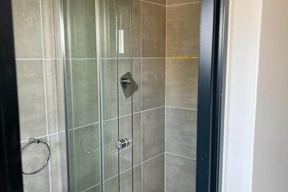 A clean, modern bathroom featuring a glass-enclosed shower with neutral wall and floor tiling.