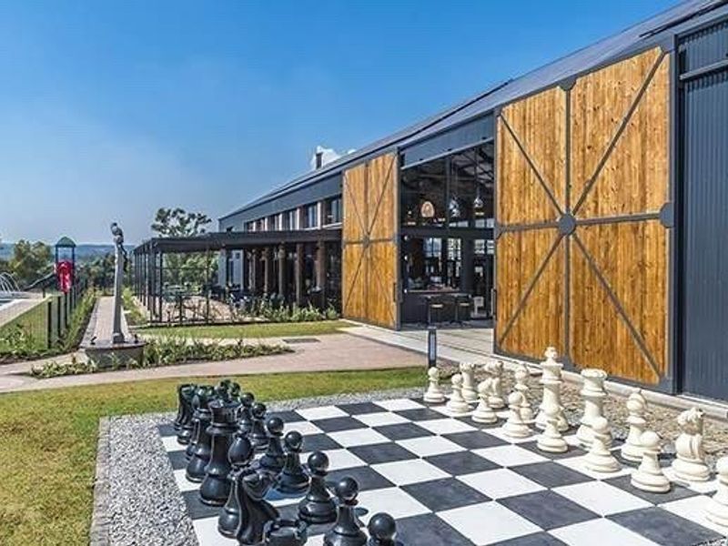 Modern clubhouse exterior featuring large sliding timber barn doors, expansive glass walls, a paved patio area, and access to a swimming pool.