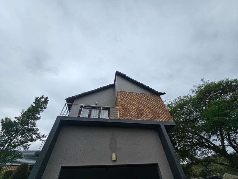 A low-angle view of the rear elevation featuring a modern balcony with metal railings, textured brick accents, and a tiled roof.
