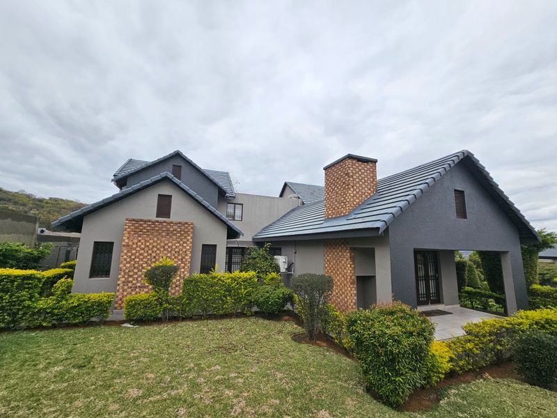 A well-maintained rear elevation of a modern house featuring a tiled roof, brick chimney accents, and a covered patio overlooking a landscaped garden.