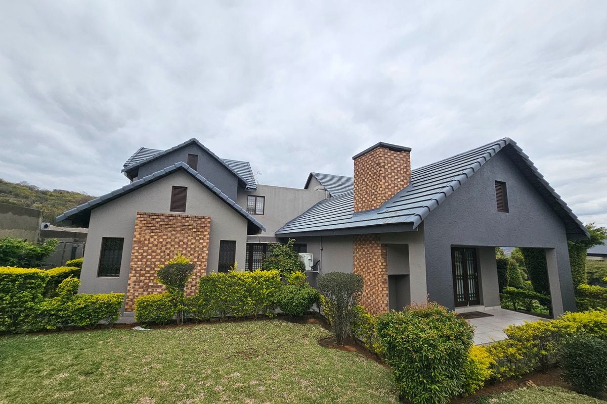 A well-maintained rear elevation of a modern house featuring a tiled roof, brick chimney accents, and a covered patio overlooking a landscaped garden.