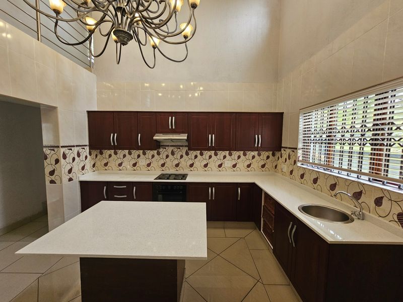 Spacious kitchen featuring dark wood cabinetry, stone countertops, a central island, and high ceilings with a decorative chandelier.