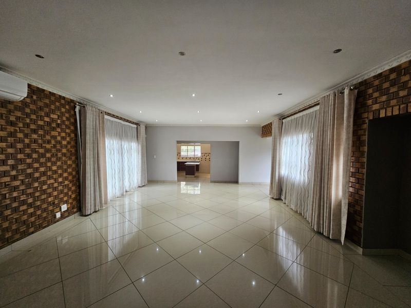 Spacious open-plan living area featuring polished tile flooring, exposed brick feature walls, recessed lighting, and direct access to the kitchen area.