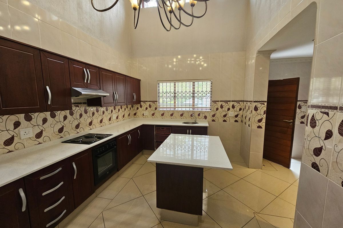 Spacious kitchen featuring dark wood cabinetry, stone countertops, a central island, built-in oven and hob, and high ceilings with decorative lighting.