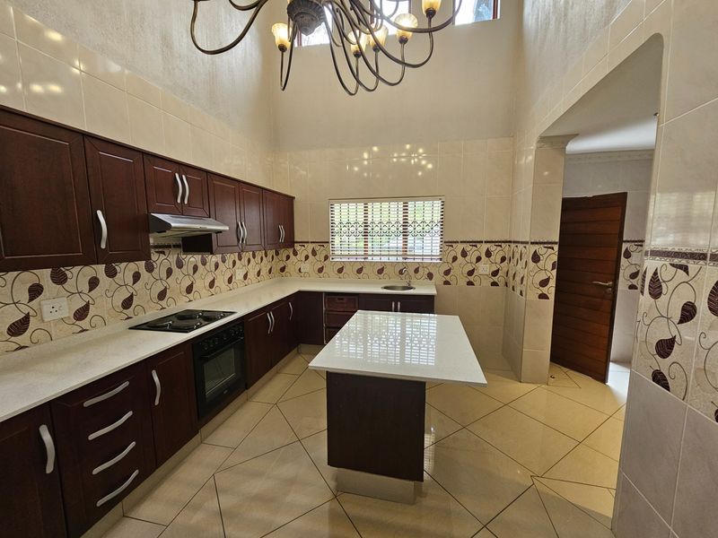 Spacious kitchen featuring dark wood cabinetry, stone countertops, a central island, built-in oven and hob, and high ceilings with decorative lighting.