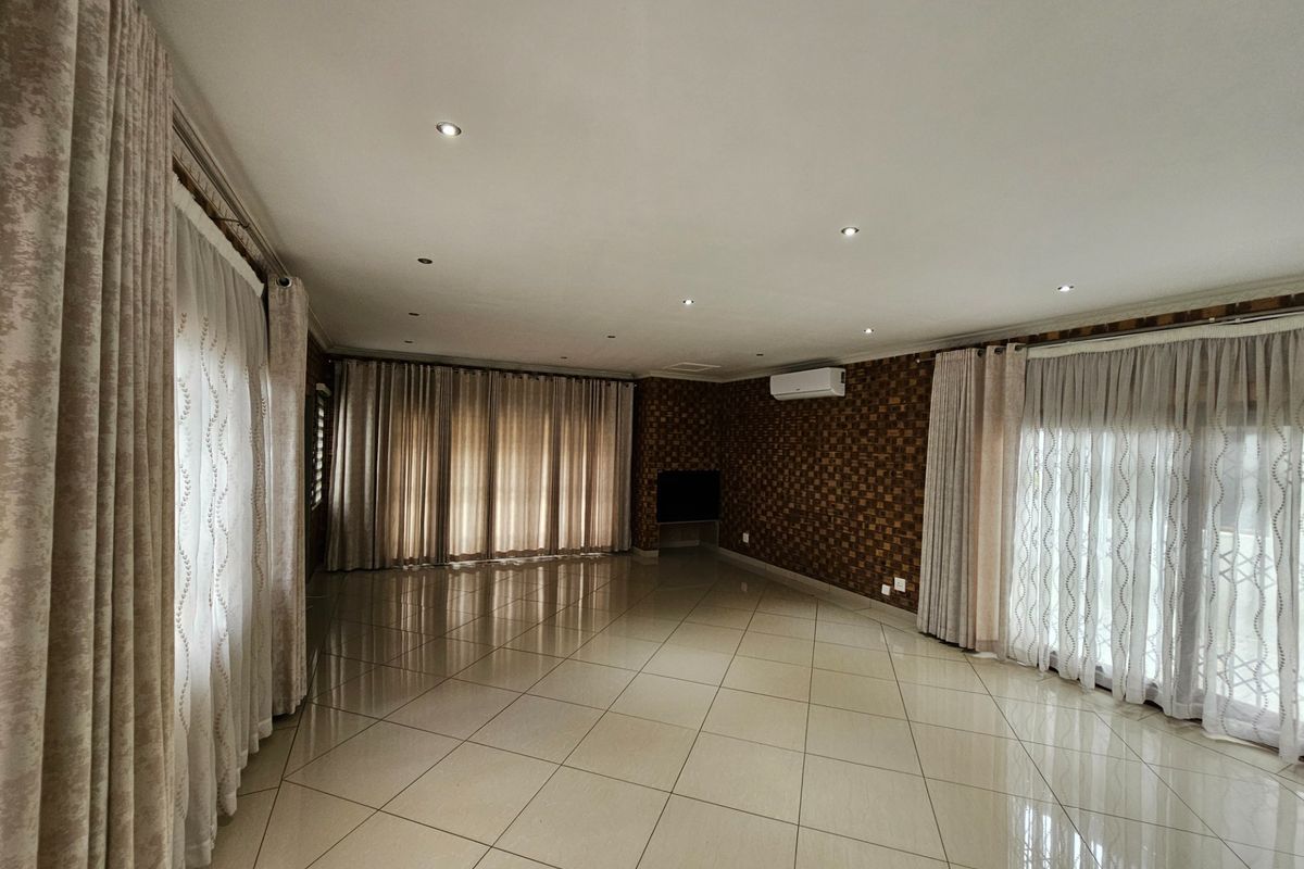 Spacious, empty living area featuring neutral tiled flooring, recessed downlighting, a wall-mounted air conditioner, and textured feature wall detailing.
