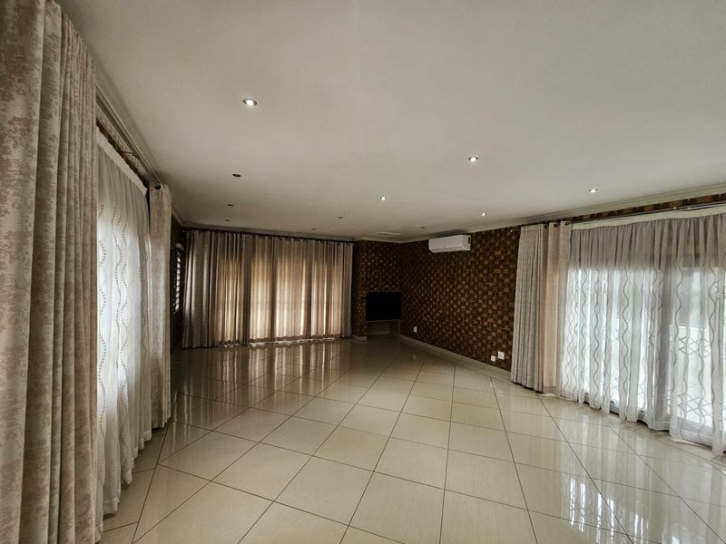 Spacious, empty living area featuring neutral tiled flooring, recessed downlighting, a wall-mounted air conditioner, and textured feature wall detailing.