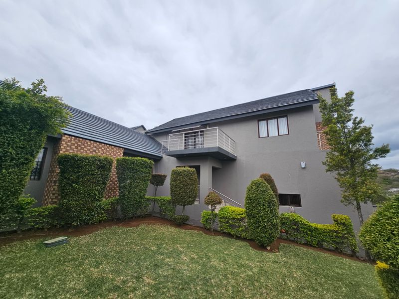 Rear view of a two-story house featuring a balcony with metal railings, a combination of brick and plastered exterior walls, and a well-maintained garden.