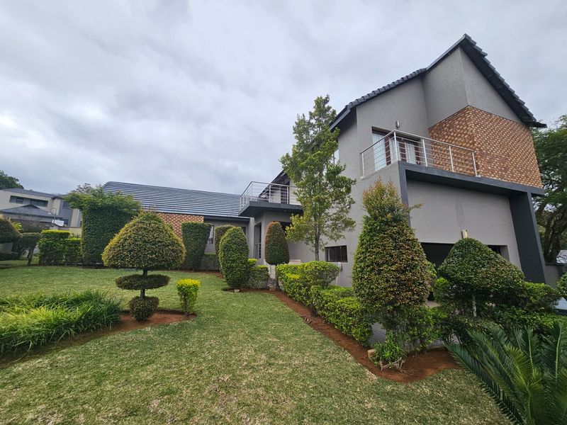 A well-maintained two-story residential property featuring a landscaped garden, balcony with metal railings, and a combination of rendered and brick facade finishes.