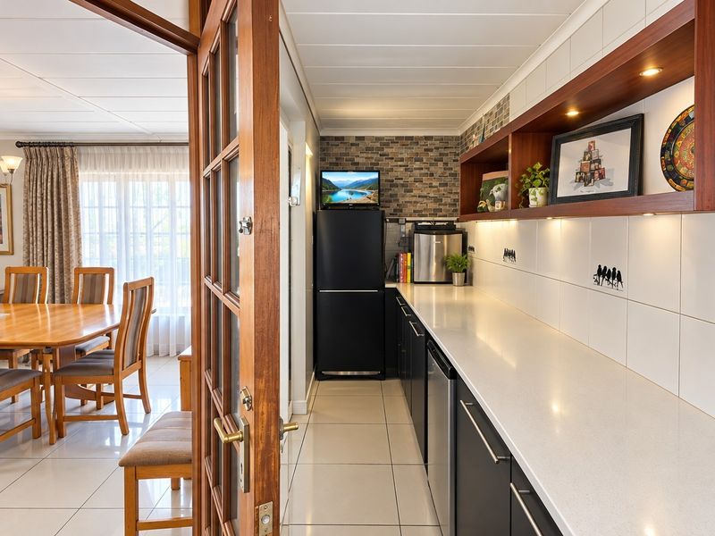 A well-maintained scullery featuring stone countertops, ample built-in cabinetry, and under-cabinet lighting, providing a functional prep and storage area adjacent to the dining room.