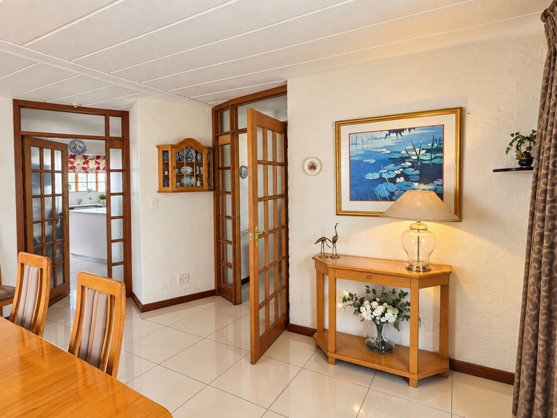 A well-maintained dining area featuring tiled flooring, textured walls, and timber-framed glass panel doors providing access to adjacent rooms.
