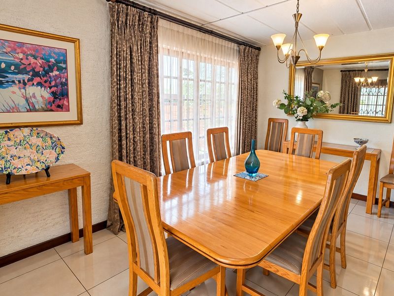 A well-maintained dining room featuring tiled flooring, a central chandelier, and a large window with curtains, providing a bright and functional space.