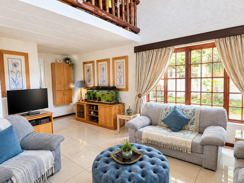 Spacious living room featuring tiled flooring, textured walls, and a mezzanine level with a timber railing, overlooking the garden through large timber-framed windows.