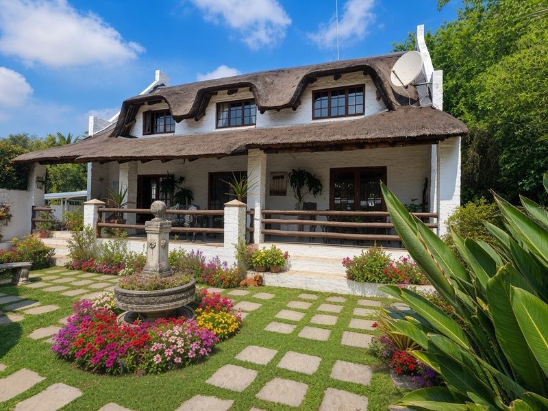 Charming cottage-style home featuring a traditional thatched roof, a covered patio, and a beautifully landscaped garden with a central stone fountain.