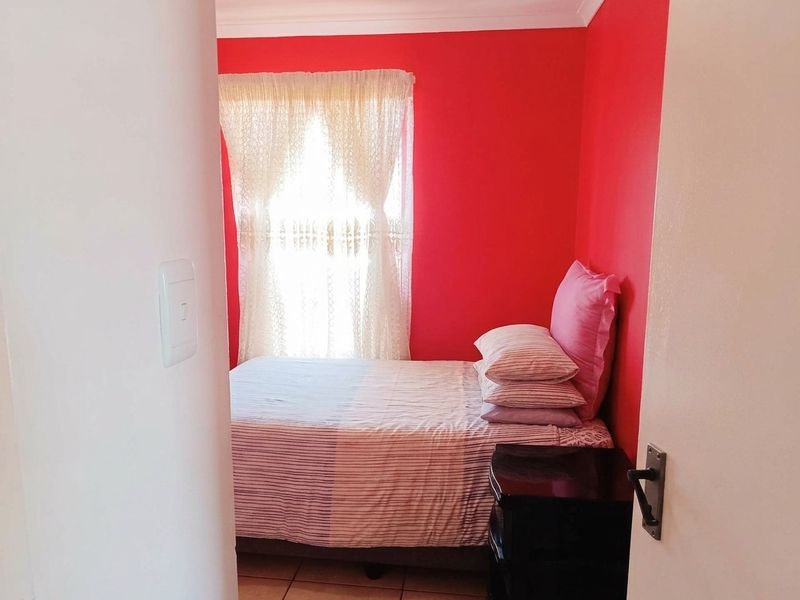 A compact bedroom featuring tiled flooring and a bold red accent wall, viewed from the doorway.