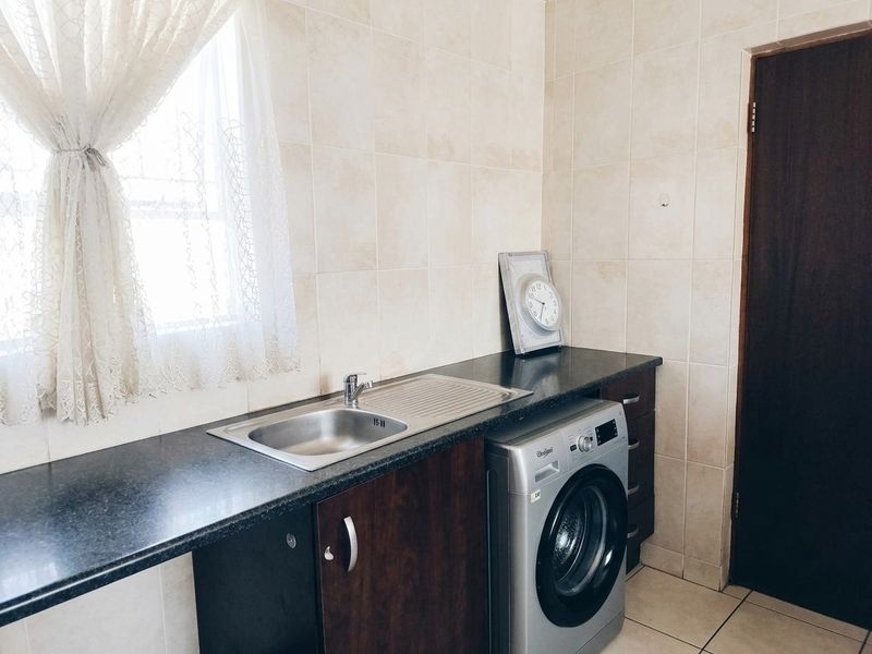 A functional laundry area featuring a stainless steel sink, dark laminate countertops, built-in cabinetry, and tiled wall finishes.