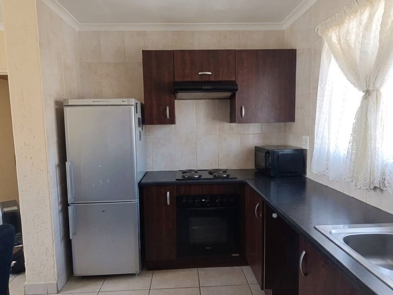 Compact kitchen featuring dark wood cabinetry, black countertops, built-in oven with hob, extractor fan, and tiled finishes throughout.