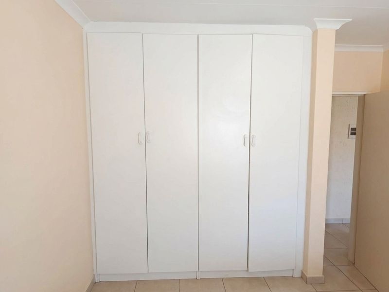 A clean bedroom space featuring a large white built-in wardrobe, neutral wall finishes, and tiled flooring.