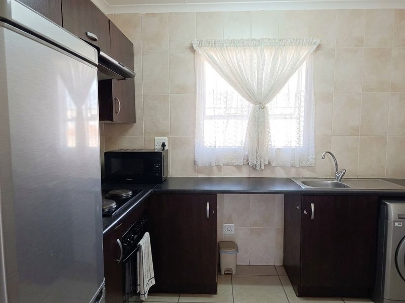 A functional kitchen featuring dark wood cabinetry, laminate countertops, a stainless steel sink, and built-in cooking appliances with tiled backsplash and flooring.