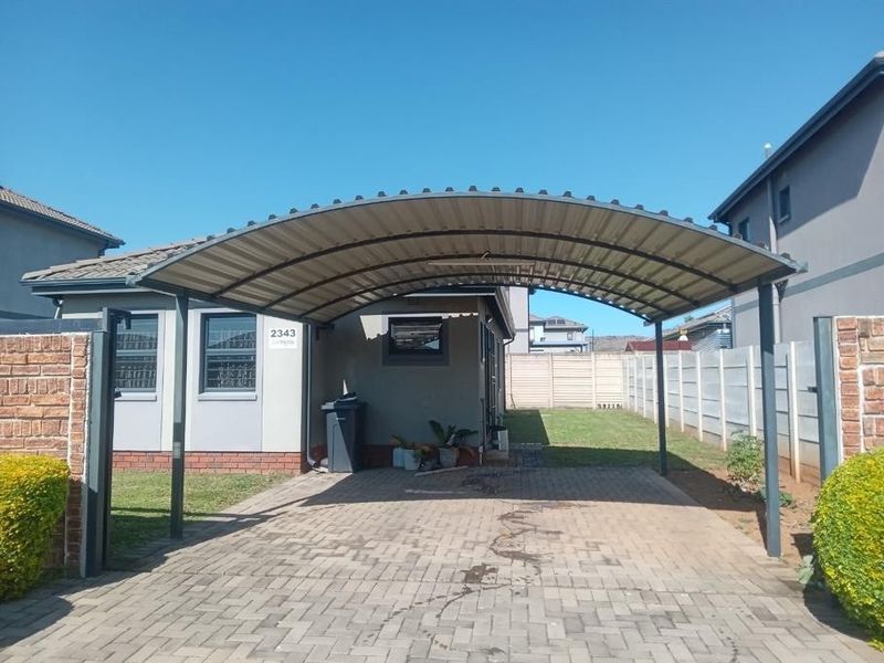 Front exterior view of the property featuring a paved driveway, a covered carport, and perimeter boundary walls.
