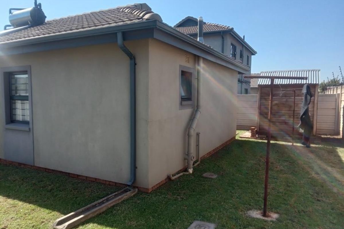 Rear exterior view of the property featuring a tiled roof, solar water heater, and a fenced garden area with a metal washing line.