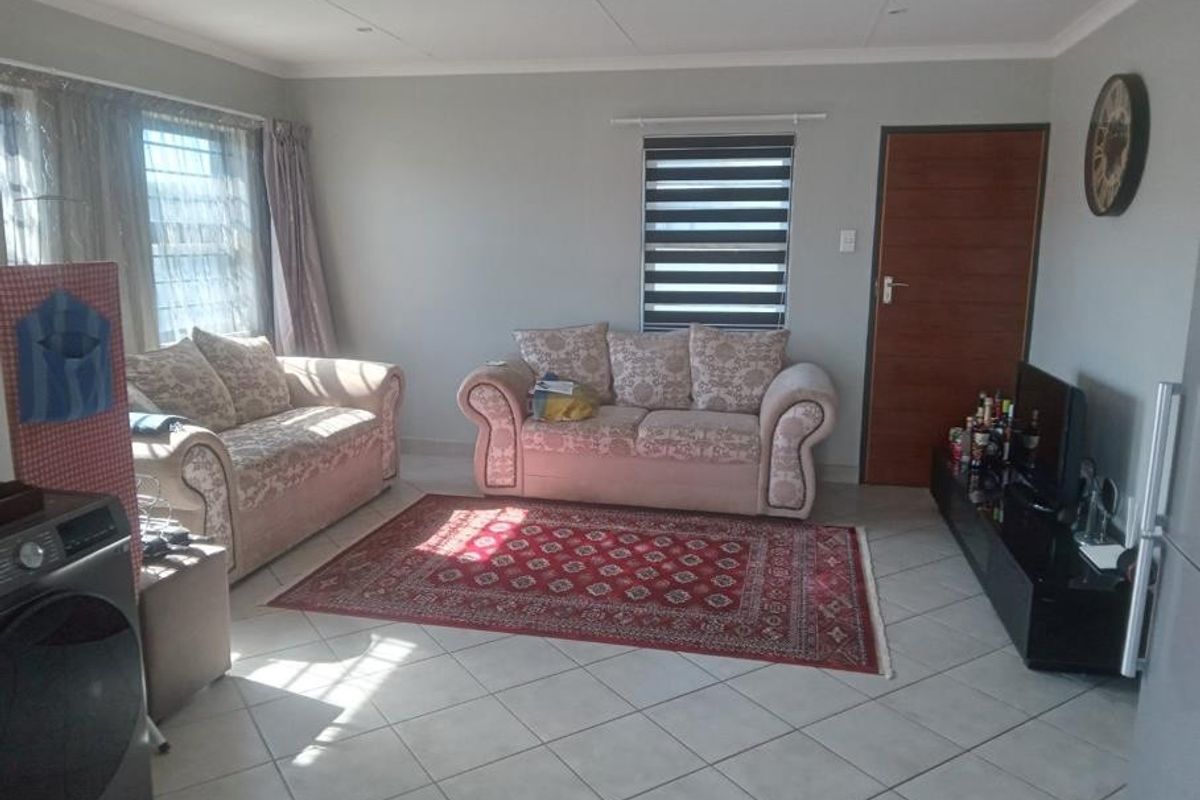 A living room featuring neutral wall tones, tiled flooring, and modern roller blinds, providing a functional and well-lit space.