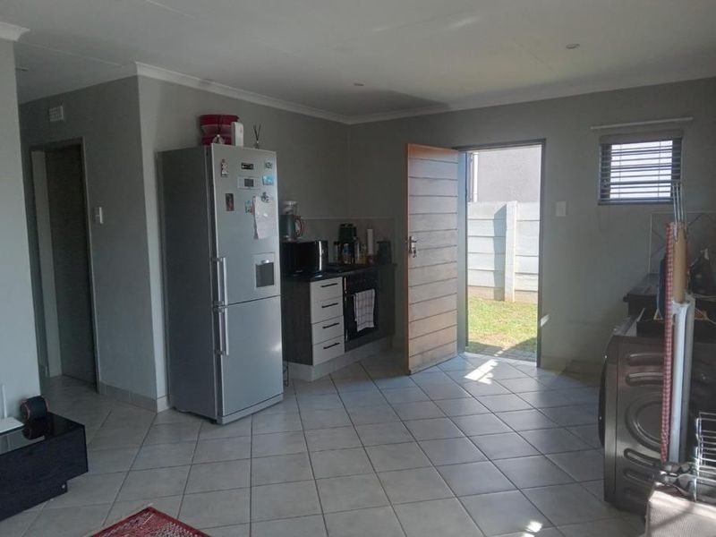 Open plan kitchen and living area featuring tiled flooring, built-in cabinetry with integrated appliances, and direct access to the rear garden.